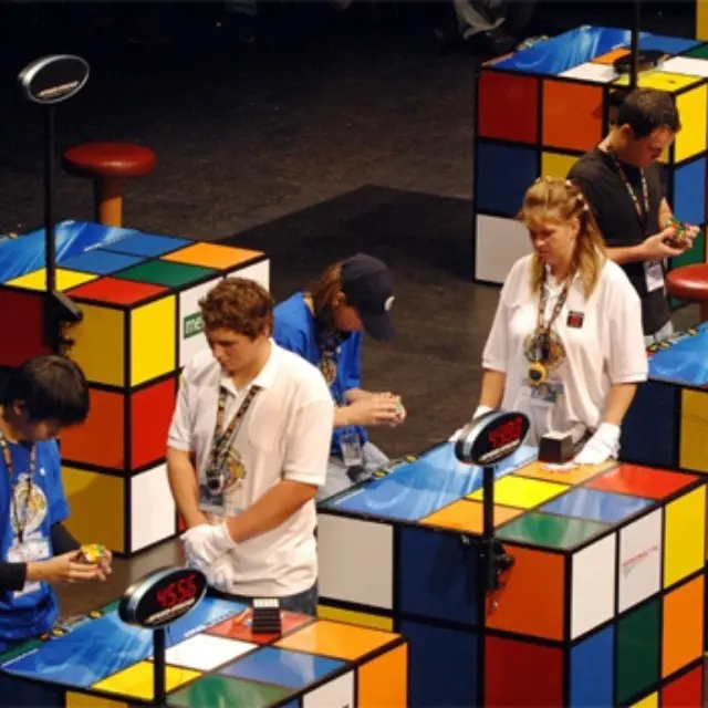 A modern speedcubing competition with rows of competitors at timed solving stations